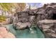 A unique pool area featuring artificial rock formations, a waterfall, and lush landscaping at 2221 S Tioga Way, Las Vegas, NV 89117
