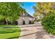 View of the brick two-car garage with an upper story and paved driveway and mature trees at 3001 Astoria Pines Cir, Las Vegas, NV 89107