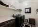Bright laundry room with wooden floor, shelving, dark cabinets, white countertop, black washer and dryer at 6225 Gambetta St, Las Vegas, NV 89115