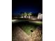 Night view of the backyard featuring lush green grass, mature trees, and brick accents at 10173 Skye Saddle Ave, Las Vegas, NV 89166