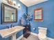 A charming bathroom features blue walls, a pedestal sink, and framed mirror with decorative lighting at 1276 Spanish Armada Rd, Las Vegas, NV 89123
