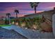 Beautiful stone-paved backyard with grass, desert vegetation, and a brick wall at dusk at 6945 Trevelez St, Las Vegas, NV 89149