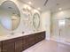 Modern bathroom featuring dual sinks, sleek cabinetry, oval mirrors, and a glass-enclosed shower at 72 Reverie Heights Ave, Henderson, NV 89011