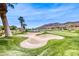 Beautiful golf course view with sand trap, vibrant green fairway, palm trees, and mountain backdrop at 11593 Glowing Sunset Ln, Las Vegas, NV 89135