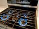 Close-up of a modern, four-burner gas stove with lit blue flames on a black and stainless steel finish at 2844 Alenga St, Henderson, NV 89044