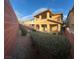 View of a private backyard featuring green bushes, rocks, and a two-story beige house with balconies and a covered patio at 5361 Candlespice Way, Las Vegas, NV 89135