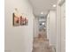 Hallway with neutral walls, plush carpet, and decorative wall art leading into a brightly lit area at 7717 Rosebark Cliffs St, North Las Vegas, NV 89084