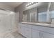 Bathroom with a double sink vanity, white cabinets, gray countertop, a glass door shower, and a large mirror at 4625 Ridgeley Ave # 103, North Las Vegas, NV 89084
