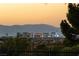 A picturesque cityscape at sunset featuring clear views of downtown and surrounding mountains, seen through landscaped greenery at 66 Golf Estates Dr, Las Vegas, NV 89141