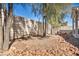 An empty backyard is filled with pea gravel, a stone retaining wall, and two shade trees under a clear blue sky at 8732 Majestic Pine Ave, Las Vegas, NV 89143
