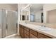 A bathroom with a glass shower, double vanity, wood cabinets, and a vanity mirror at 10632 Open Range Ct, Las Vegas, NV 89179