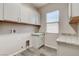 A bright laundry room featuring white cabinets, granite countertops, a stainless steel sink, and wood-look tile flooring at 7119 Falabella Ridge Ave, Las Vegas, NV 89131