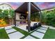 Covered outdoor living area with a fireplace, tv, and lounge seating surrounded by greenery at 3929 Reyes Ave, Las Vegas, NV 89141