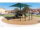 Community playground with shade cover and wood chip base with homes in background at 6891 Nickel Mine Ave, Las Vegas, NV 89122
