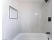 A modern bathroom with sleek, light marble-style tiling and dark fixtures, a built-in shelf, and a soaking tub at 1009 N Tenaya Way, Las Vegas, NV 89128