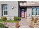 Close-up of a home's entrance featuring a modern red door, lush landscaping, and brick walkway leading to the front door at 9938 Regency Canyon Way, Las Vegas, NV 89148