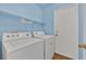 Bright laundry room with modern washer and dryer units, white shelving, and access door at 8468 W Gilmore Ave, Las Vegas, NV 89129