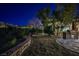 Backyard landscaping featuring a built-in grill, stone patio, mature trees, desert plants, and starlit sky at twilight at 3163 Elk Clover St, Las Vegas, NV 89135