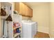 This laundry room features a washer and dryer, storage cabinets, tile floors, and cleaning supplies at 7172 Painted Paradise St, Las Vegas, NV 89131