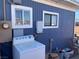 An exterior view of the side of the home showing blue wood siding, windows, a chair, and a washer at 11 Magnesium St, Henderson, NV 89015