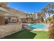 A beautiful pool with a waterfall feature and a covered patio with an outdoor kitchen, surrounded by lush greenery at 3680 Belvedere Park Ln, Las Vegas, NV 89141
