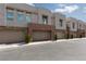 A view of garages in modern townhomes, featuring neutral paint, stone accents, and small, manicured trees at 600 N Carriage Hill Dr # 1081, Las Vegas, NV 89138
