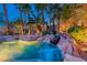 Backyard swimming pool with a rock waterfall, lush landscaping, and lighting at 1983 Songbird Ct, Henderson, NV 89012