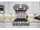 Close-up of a stainless steel stove and range hood with white cabinets and marble countertops at 47 Grand Masters Dr, Las Vegas, NV 89141