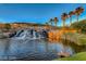 Picturesque waterfall cascading into a serene pond, framed by lush greenery and palm trees, creating a tranquil oasis at 21 Via Visione # 101, Henderson, NV 89011