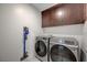 Modern laundry room featuring gray front-load washer and dryer, with dark wood cabinets and a vacuum at 2685 Conifer Canyon St, Henderson, NV 89044