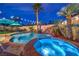 A serene backyard oasis with a pool, spa, rock waterfall, and lush palm trees at twilight at 8032 Marbella Cir, Las Vegas, NV 89128