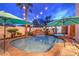 A serene backyard oasis with a pool, spa, rock waterfall, and lush palm trees under lights at twilight at 8032 Marbella Cir, Las Vegas, NV 89128