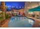 A serene backyard oasis with a pool, spa, rock waterfall, and lush palm trees with lights at twilight at 8032 Marbella Cir, Las Vegas, NV 89128