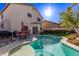 An in-ground backyard pool featuring a large patio with an outdoor dining set, and lush green shrubbery at 9020 Loggers Mill Ave, Las Vegas, NV 89143