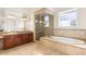 A full primary bathroom featuring a soaking tub, walk-in shower, dual sink vanity, and travertine tile flooring at 2660 Mirabella St, Henderson, NV 89052