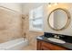 Bright bathroom featuring tan tiled walls, a tub and shower combo, and a vanity with a black countertop at 2660 Mirabella St, Henderson, NV 89052