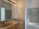 Bathroom with a double sink vanity, a large mirror with vanity lighting and a bathtub with gray marbled tile surround at 8244 Sickle Ln, Las Vegas, NV 89128