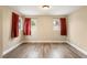 Empty bedroom features hardwood floors and three windows with dark red curtains at 6858 Groveview Ln, Las Vegas, NV 89103