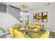 Bright dining room with glass table, stylish yellow seating, chandelier, and staircase, perfect for entertaining at 7925 Limbwood Ct, Las Vegas, NV 89131