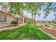 Well-manicured backyard with green lawn, covered patio, mature trees, and views of the surrounding landscape at 138 Wentworth Dr, Henderson, NV 89074