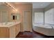 Bright bathroom featuring double sinks, wood cabinets, and a large soaking tub by the window at 8980 High Horizon Ave, Las Vegas, NV 89149
