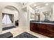 Bright bathroom featuring travertine floors, granite counters, vanity with seating area, and decorative arched doorway at 10412 Mansion Hills Ave, Las Vegas, NV 89144