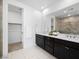 Dual sink bathroom with dark cabinets, tiled floor and frameless glass shower with walk-in closet access at 7222 Pulsar Mesa Ct, Las Vegas, NV 89148