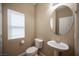 Cozy powder room featuring a pedestal sink, toilet, and oval mirror, complemented by a window at 10643 Petricola St # 103, Las Vegas, NV 89183