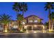Beautiful two-story home with a three-car garage and palm trees lining the front at twilight at 2232 Barchetta Dr, Las Vegas, NV 89134