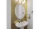 Stylish powder room featuring a pedestal sink, decorative mirror, and metallic gold wall tiles at 11834 Albissola Ave, Las Vegas, NV 89138