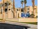 A tan stucco complex entry featuring mature palm trees and an identifying 