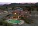 Aerial view of home with covered patio, pool with lights, and mountain views in the background at 5690 N Park St, Las Vegas, NV 89149
