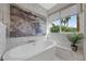 Bright bathroom features a soaking tub next to a window with views of palm trees and a modern art piece at 1912 Calanda Ct, Las Vegas, NV 89102