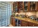 A stylish wet bar boasts rich wood cabinetry, granite countertops, and a glass block wall for a unique design element at 2994 San Lorenzo Ct, Henderson, NV 89052